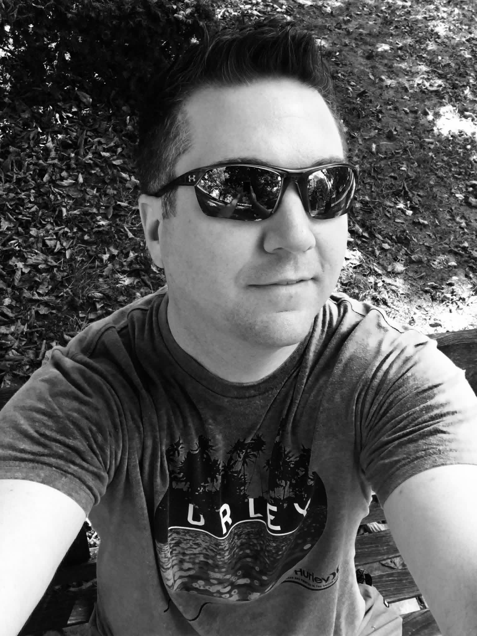 A black-and-white selfie of Shane in sunglasses and a Hurley T-shirt, outdoors.