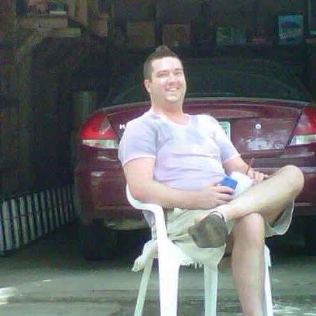 Shane relaxing in a lawn chair in the driveway on a summer day, drink in hand.