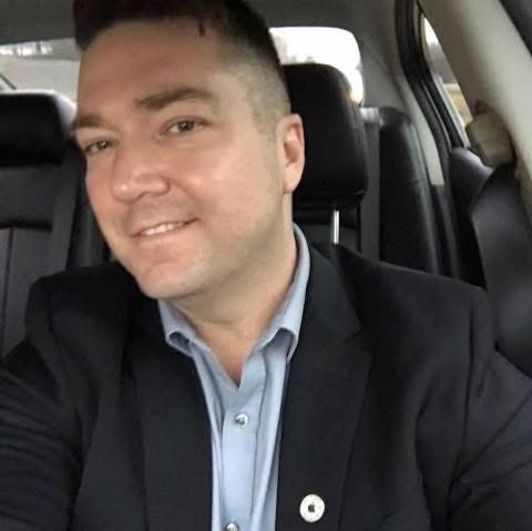 Shane dressed up in a suit with an Apple pin on the lapel, taking a selfie in the car.
